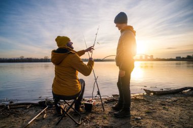 Father and son are fishing on winter day. River fishing. Teenage boy is learning to fish.
