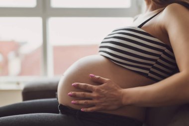 Pregnant woman relaxing at home. She is sitting on bed in bedroom. clipart