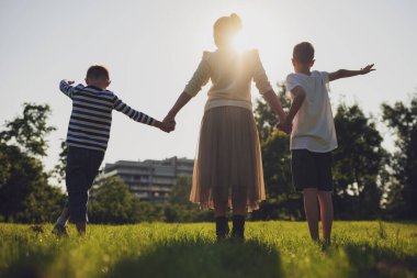 Mutlu anne parkta oğullarıyla oynuyor. El ele tutuşup günbatımının tadını çıkarıyorlar..