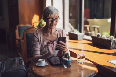 Olgun bir kadın havaalanındaki bir kafede oturmuş uçağa binmeyi bekliyor. Akıllı telefondan programı inceliyor..