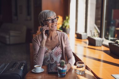 Olgun bir kadın havaalanındaki bir kafede oturmuş uçağa binmeyi bekliyor..