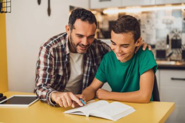 Baba oğluna öğrenmesinde yardım ediyor. Birlikte ödev yapıyorlar..