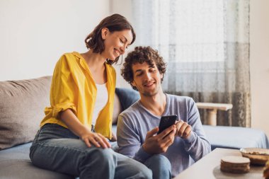 Evde akıllı telefona bakan mutlu genç bir çiftin portresi..