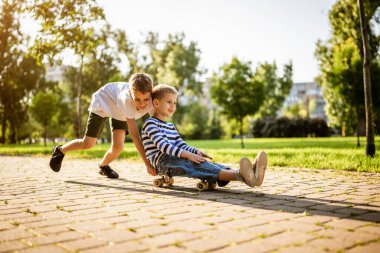 İki çocuk parkta kaykayla eğleniyor. Parkta neşeli çocuklar, mutlu bir çocukluk..