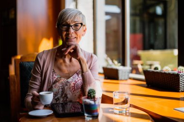 Olgun kadın kafede oturuyor ve dinleniyor. Kahve içiyor..