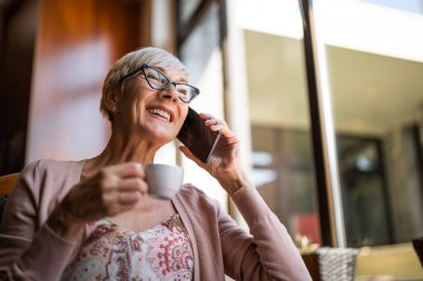 Olgun kadın kafede oturuyor ve dinleniyor. Telefonla konuşuyor..