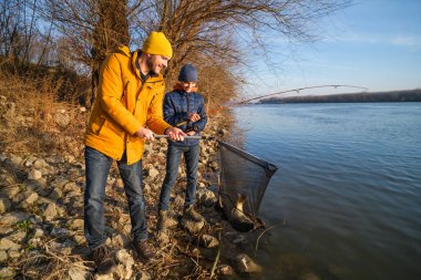 Father and son are fishing on sunny winter day. They caught a fish and are holding it in a landing net.