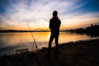 Teenage boy is fishing on river bank. Boy is fishing in sunset.