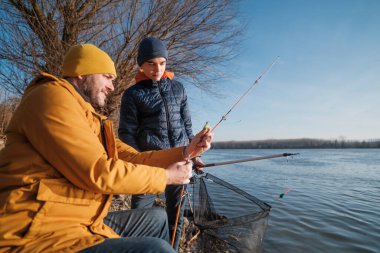 Father and son are fishing on sunny winter day. Freshwater fishing. Teenage boy is learning to fish.