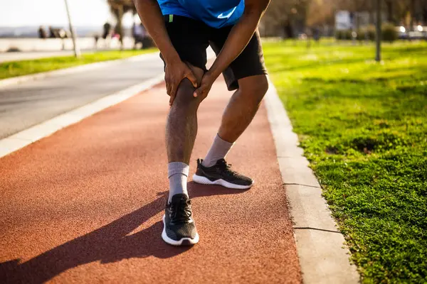 アフリカ系アメリカ人の若者がジョギング中に怪我をしている 膝に痛みがある — ストック写真