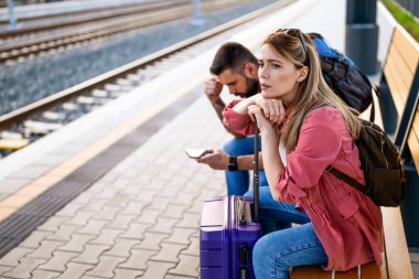 Endişeli ve yorgun bir çift tren istasyonunda oturmuş trenlerinin gelmesini bekliyor..