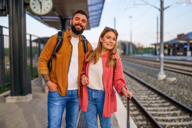 Mutlu çift tren istasyonunda duruyor ve trenlerinin gelmesini bekliyorlar..