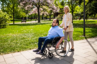 Tekerlekli sandalyedeki adam annesiyle parkta vakit geçiriyor. Birlikte güneşli bir günün tadını çıkarıyorlar..