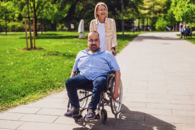 Tekerlekli sandalyedeki adam annesiyle parkta vakit geçiriyor. Birlikte güneşli bir günün tadını çıkarıyorlar..