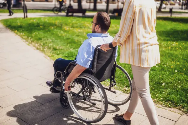 Tekerlekli sandalyedeki adam annesiyle parkta vakit geçiriyor. Birlikte güneşli bir günün tadını çıkarıyorlar..