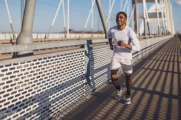 年轻的非洲裔美国人正在城里的桥上慢跑 免版税图库照片
