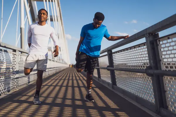 アフリカ系アメリカ人の2人の友人が市内の橋で運動している 彼らはジョギングのために温暖化しています ストックフォト