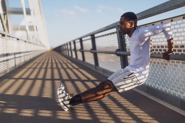 若いアフリカ系アメリカ人男性が市内の橋で運動している 彼は逆のプッシュアップをしている ストック写真