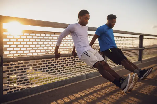 两个非洲裔美国朋友正在城里的桥上锻炼 他们在做反向俯卧撑 图库照片