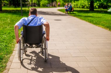 Tekerlekli sandalyedeki adam parkta yuvarlanıyor..