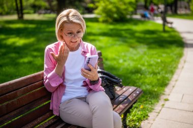 Parktaki olgun bir kadının portresi. Telefonla konuşuyor..