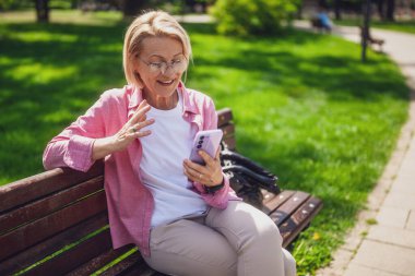 Parktaki olgun bir kadının portresi. Telefonla konuşuyor..