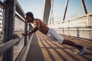 Genç Afro-Amerikalı adam, şehirdeki köprüde egzersiz yapıyor. Şınav çekiyor..