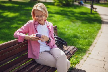 Parktaki olgun bir kadının portresi. Akıllı telefon kullanıyor..