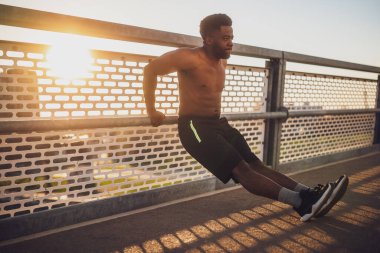 Genç Afro-Amerikalı adam, şehirdeki köprüde egzersiz yapıyor. Ters şınav çekiyor..