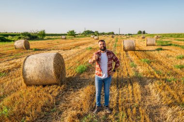 Çiftçi saman balyalarının yanında duruyor. O, başarılı bir hasattan sonra tatmin olur..