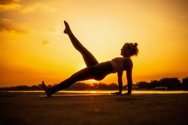 Gün batımında pilates uygulayan kadın. Bacak geri çekme egzersizi.