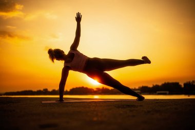 Gün batımında pilates uygulayan kadın. Bacak tekme egzersizi ile yan tahta.