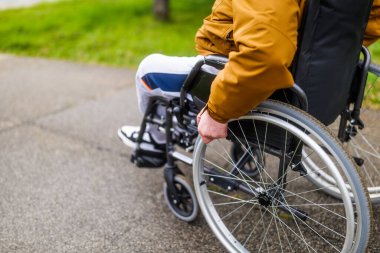 Parktaki tekerlekli sandalyedeki felçli sakat adamın yakın plan görüntüsü. Patikada yuvarlanıyor..