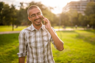 Parkta telefonla konuşan neşeli bir yetişkinin portresi..