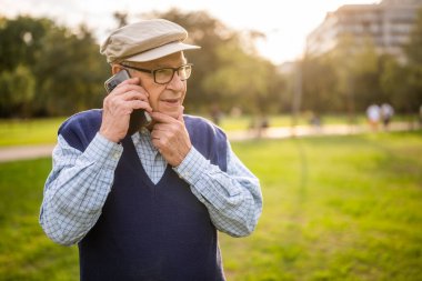 Güneşli bir günde parktaki endişeli yaşlı adamın portresi. Cep telefonuyla konuşuyor..