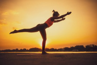 Gün batımında yoga yapan bir kadın. Virabhadrasana, Savaşçı 3 poz