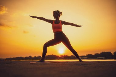 Gün batımında yoga yapan bir kadın. Virabhadrasana, Savaşçı 2 poz
