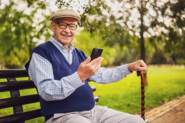 Park 'taki mutlu son sınıf öğrencisinin portresi. Bankta oturuyor ve akıllı telefon kullanıyor..