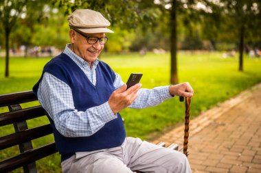 Park 'taki mutlu son sınıf öğrencisinin portresi. Bankta oturuyor ve akıllı telefon kullanıyor..