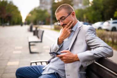 Telefonda mesajlaşan dalgın iş adamının portresi. Şehirde bankta oturan ve akıllı telefon kullanan bir adam..