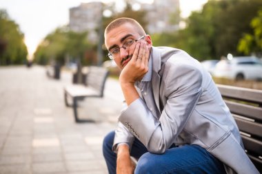 Düşünceli ve endişeli bir adamın portresi. Kentte bankta oturuyor ve düşünüyor..