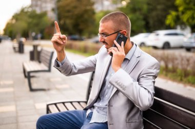 Telefonda konuşan hayal kırıklığına uğramış iş adamının portresi. Şehirde bankta oturan ve telefonla konuşan bir adam..