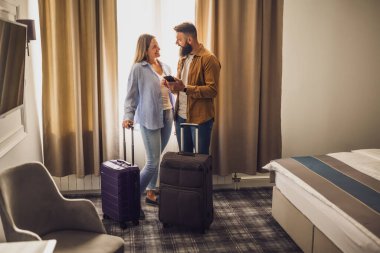 Genç mutlu çift tatilde. Turistler bavullarıyla otel odasına geldiler..