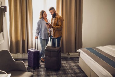 Genç mutlu çift tatilde. Turistler bavullarıyla otel odasına geldiler..