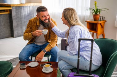 Genç mutlu çift tatile çıkıyor. Turistler otel lobisinde oturup kahve içiyorlar..