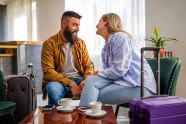 Genç mutlu çift tatile çıkıyor. Turistler otel lobisinde oturup kahve içiyorlar..