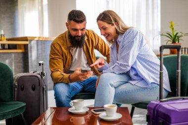 Genç mutlu çift tatile çıkıyor. Turistler otel lobisinde oturup kahve içiyorlar..