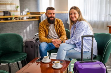 Genç mutlu çift tatile çıkıyor. Turistler otel lobisinde oturup kahve içiyorlar..