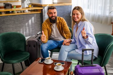 Genç mutlu çift tatile çıkıyor. Turistler otel lobisinde oturup kahve içiyorlar..