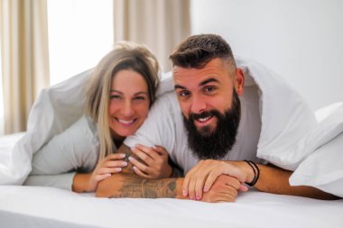 Genç ve mutlu bir çift sabahları yatakta yatıyor. Eğleniyorlar ve gülümsüyorlar..